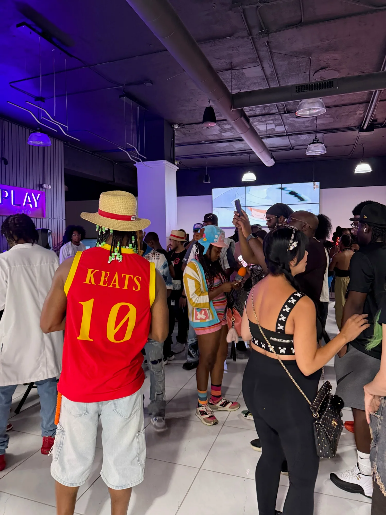 Fans wearing One Piece-inspired hats and outfits gather inside Sole Play under purple lighting